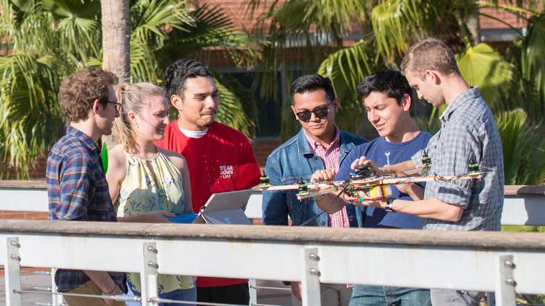 Five University of Arizona students are gather around a hand-made drone and iPad before testing its flight capabilities.