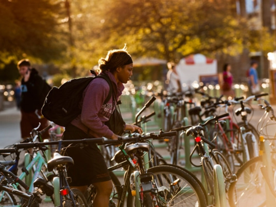 Student parking a bicycle on the bike rack with the sun setting in the background