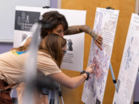 two people pointing at a posted board with a map on it